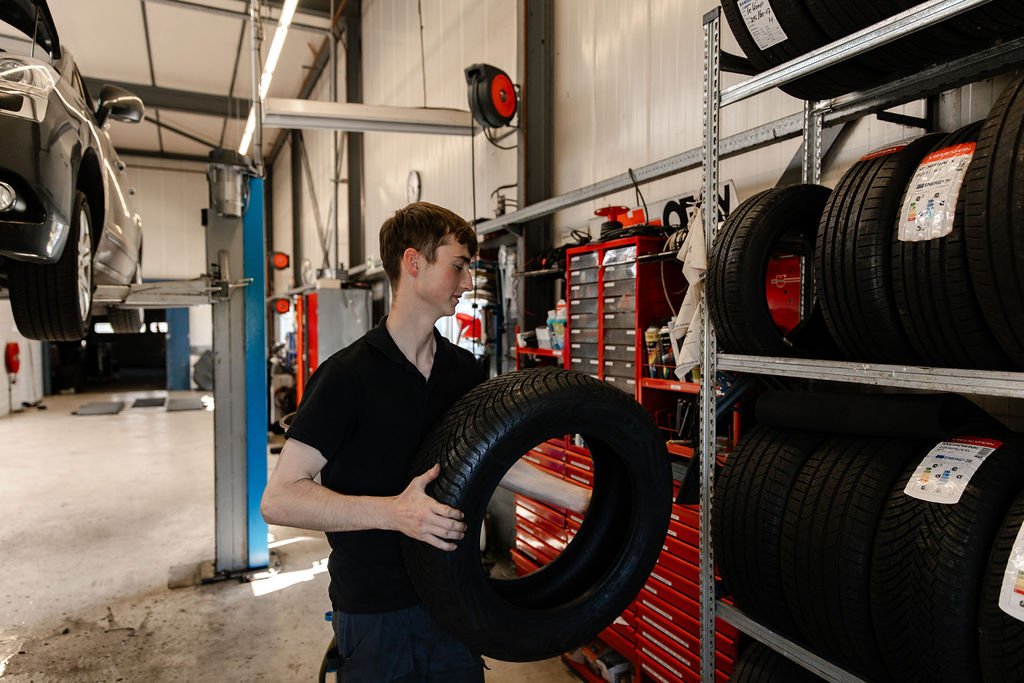 Monteur met autoband in zijn handen in een autogarage